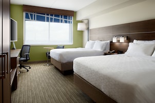 A hotel room with two beds, a desk, a chair, a TV, and a window with blinds.