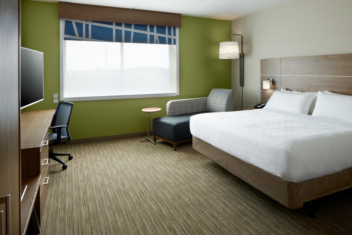 A hotel room with a large bed, a desk with a chair, a small round table, and a TV.