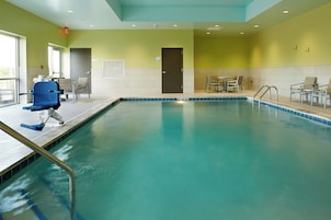 A swimming pool with a blue border, a chair, and a table with chairs around it.