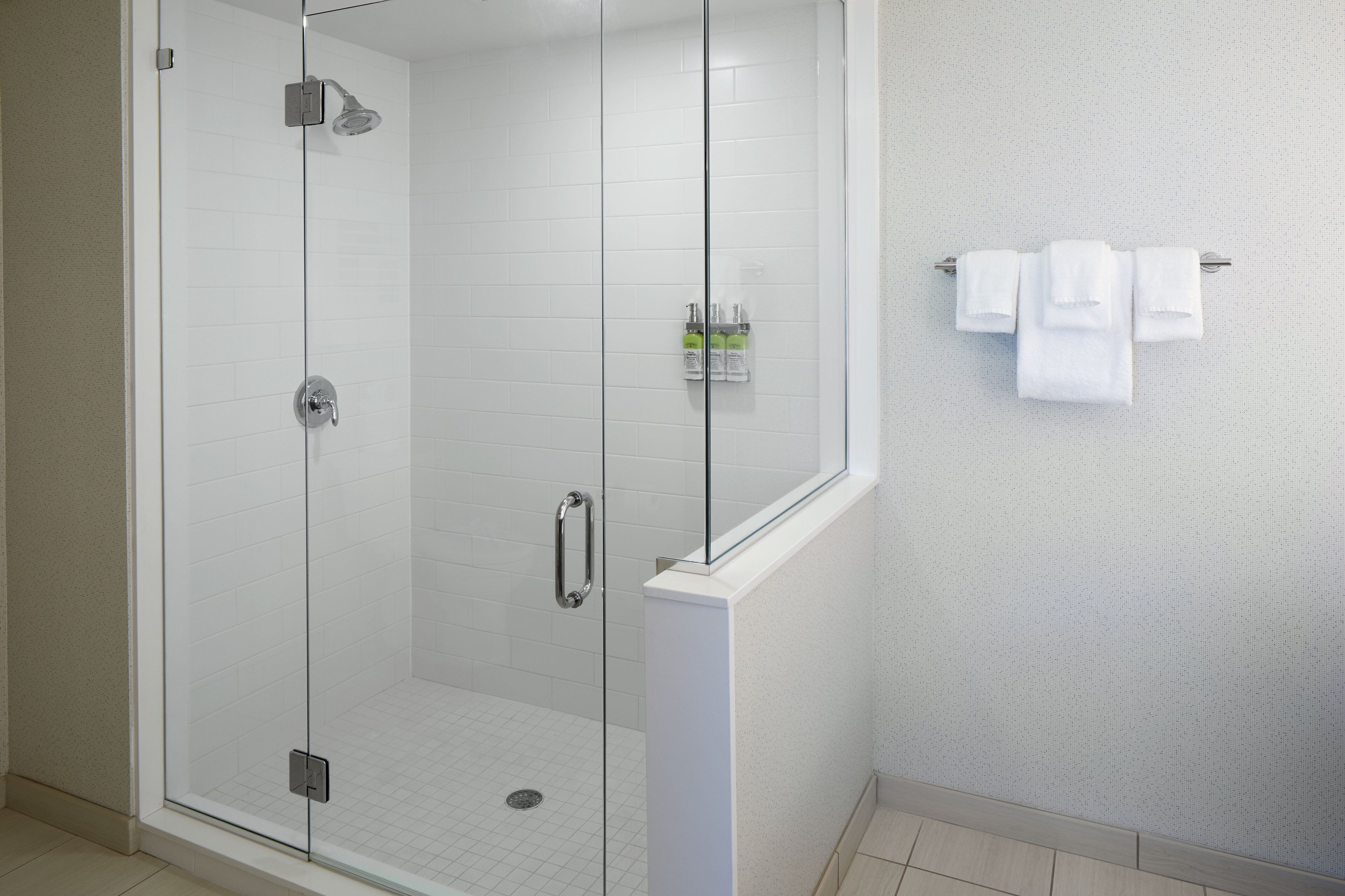 Ducha envuelta en vidrio con cabezal de ducha de mano, puerta de cristal y piso de azulejos.