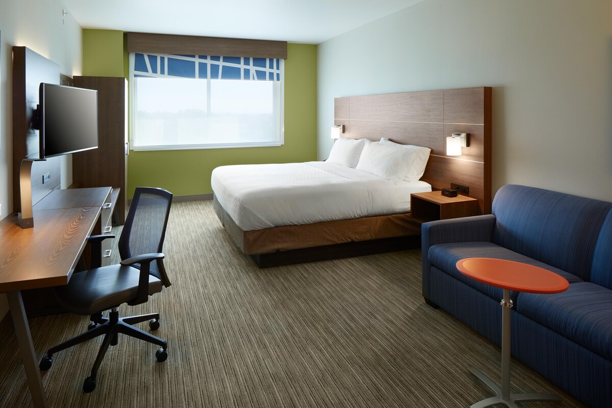 A hotel room with a bed, a desk with a chair, a television, a nightstand, and a sofa.