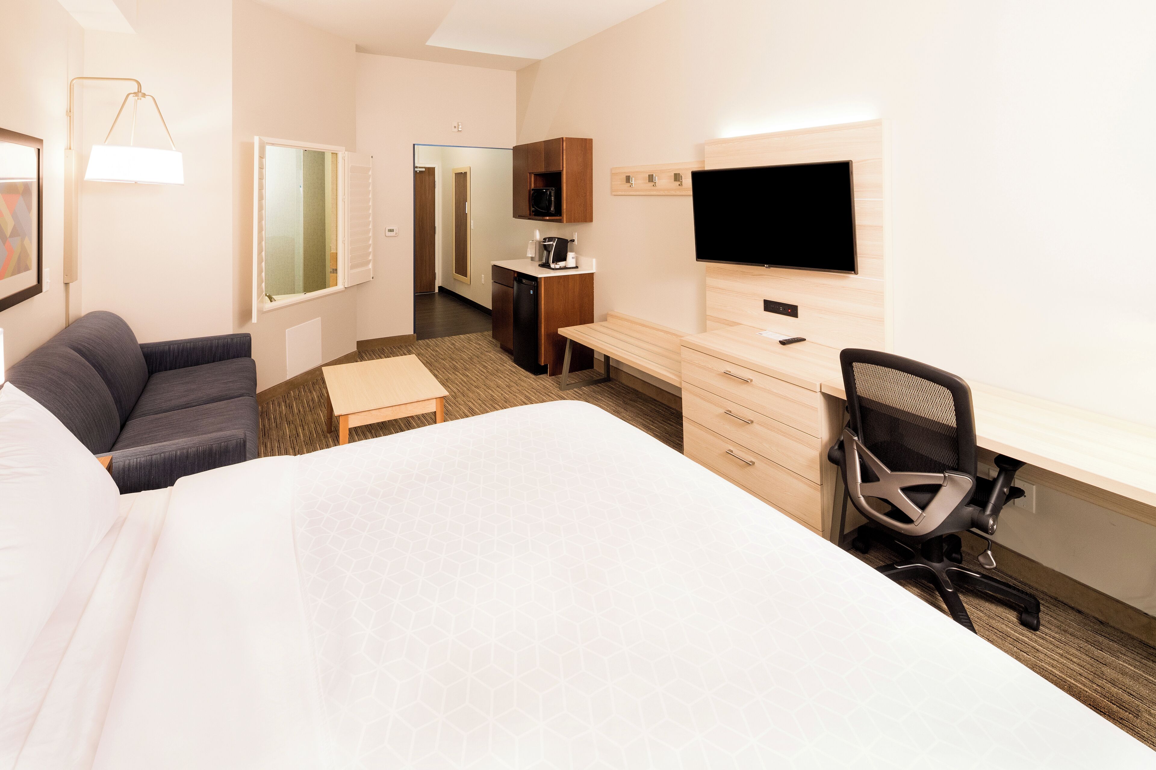 Ein Hotelzimmer mit einem großen Bett, einem Schreibtisch mit Stuhl, einem Fernseher, einer Mikrowelle und einer kleinen Küchenzeile.
