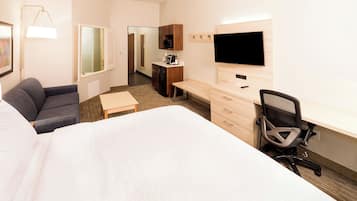Ein Hotelzimmer mit einem großen Bett, einem Schreibtisch mit Stuhl, einem Fernseher, einer Mikrowelle und einer kleinen Küchenzeile.