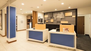 A reception area with two blue and white reception desks, a wall-mounted clock, and a door to the right.