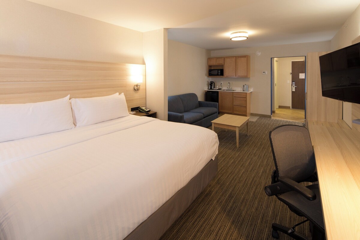 Ein Hotelzimmer mit einem großen Bett, einem Schreibtisch mit Stuhl, einer Sitzecke, einem Fernseher, einer Mikrowelle und einer Küchenzeile.