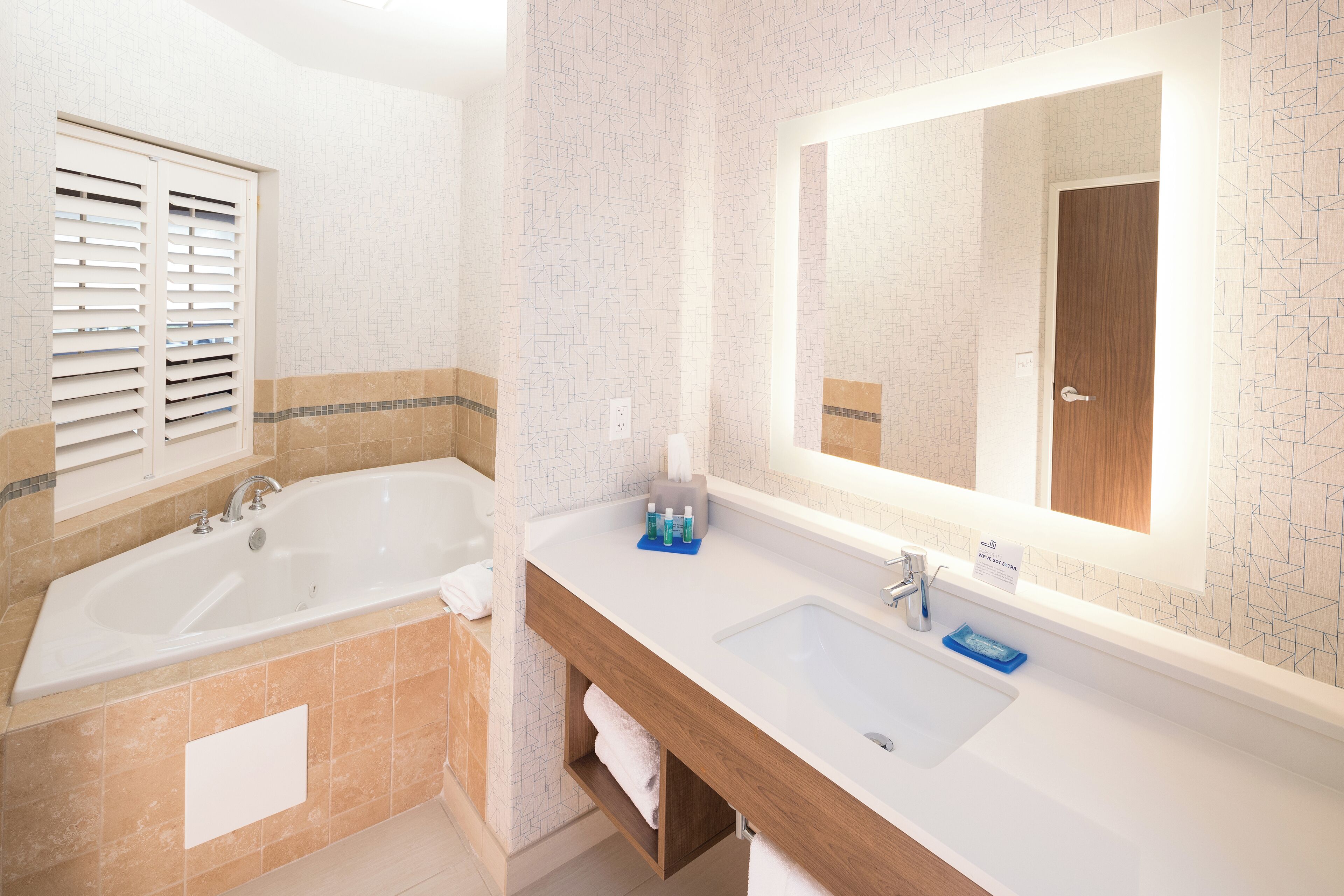 A modern bathroom with a large bathtub, a vanity with a mirror, and a tiled backsplash.