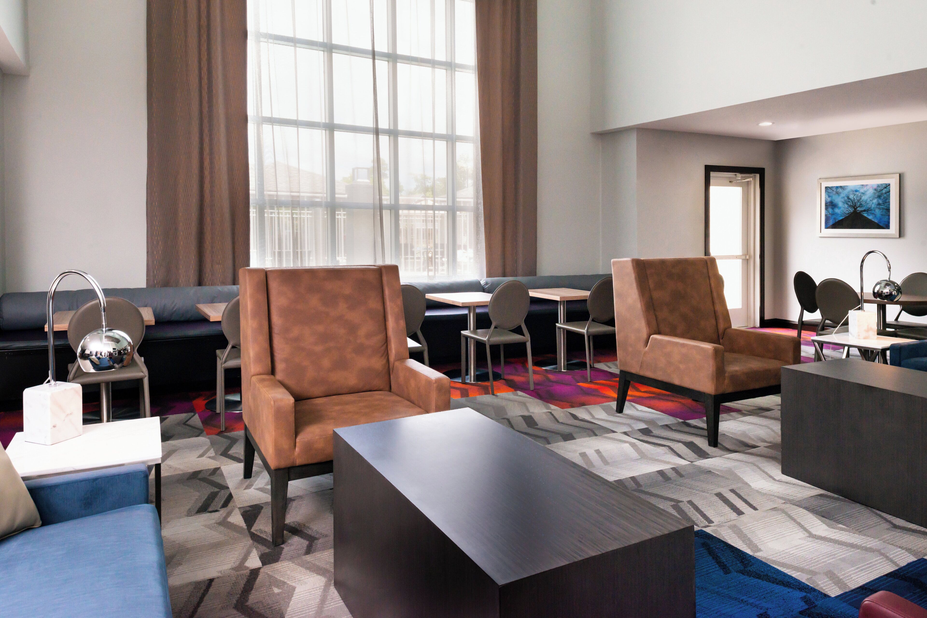 A modern hotel lobby with leather armchairs, a sofa, a coffee table, and a dining area with chairs and a table.