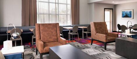 A modern hotel lobby with leather armchairs, a sofa, a coffee table, and a dining area with chairs and a table.