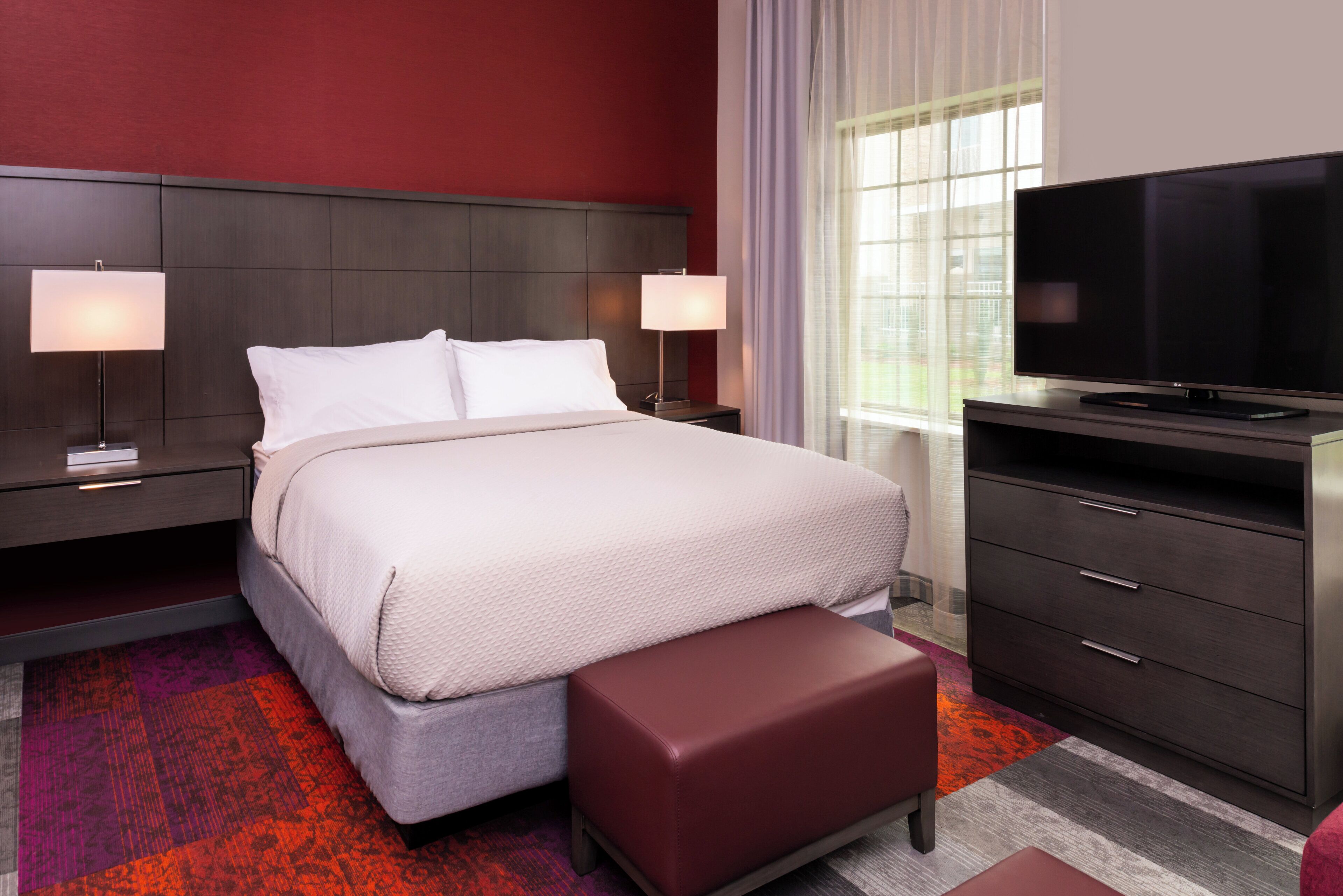 A hotel room with a bed, bedside tables, a TV, and a dresser.