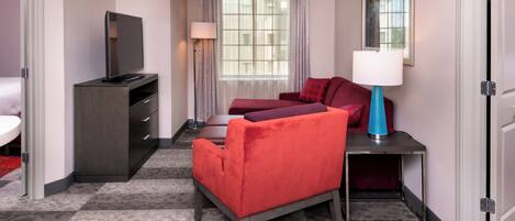 Une chambre d’hôtel avec un lit, un bureau avec une lampe, une télévision et une fenêtre avec des rideaux.