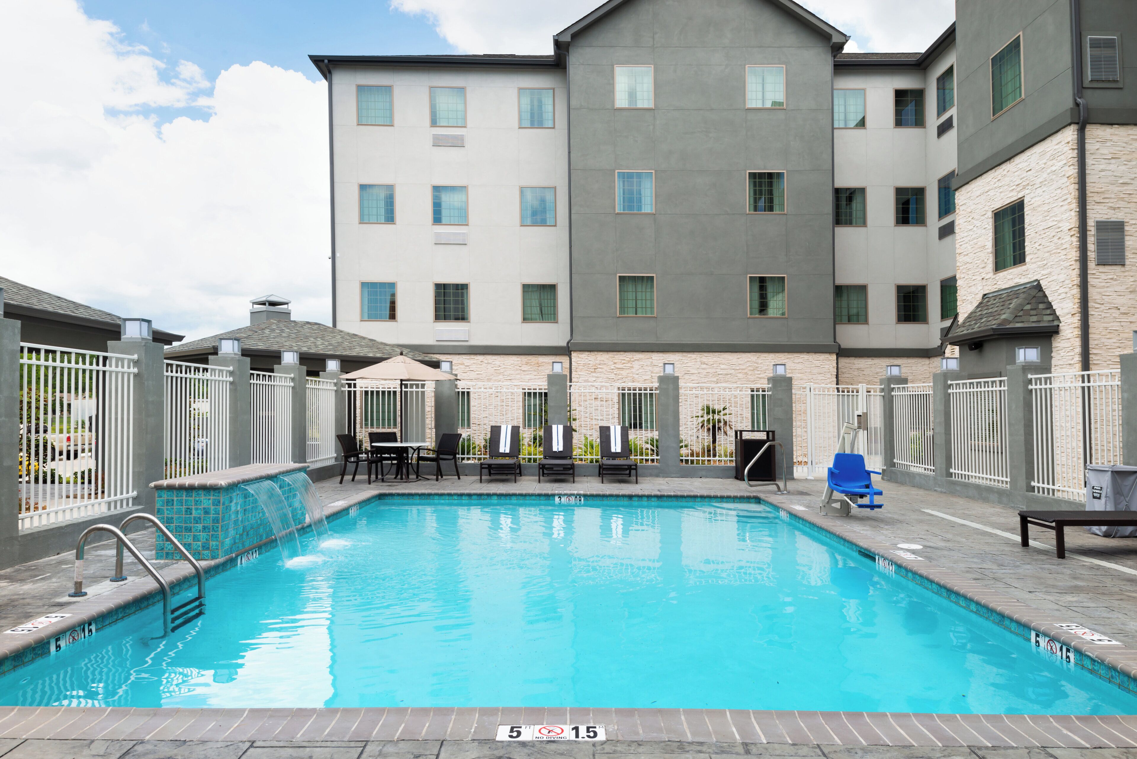 A swimming pool with lounge chairs and a building with multiple windows in the background.