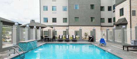 A swimming pool with lounge chairs and a building with multiple windows in the background.