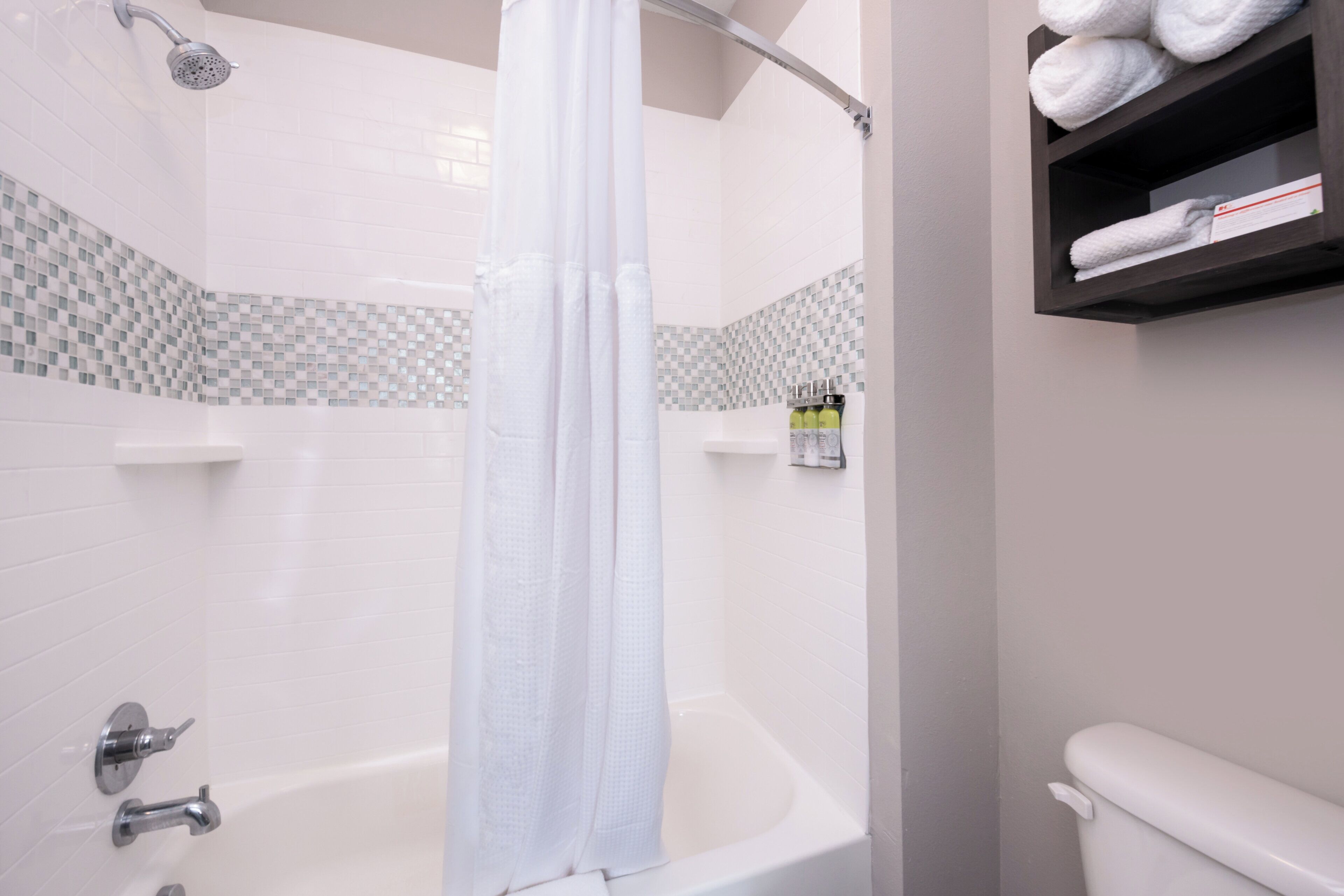 Un baño con bañera, ducha e inodoro. Hay toallas en un estante.