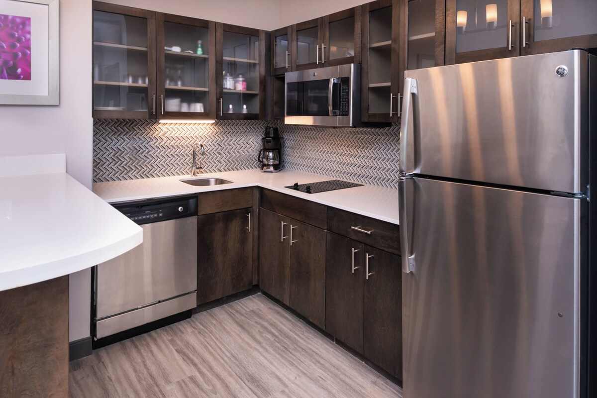 A modern kitchen with stainless steel appliances, wooden cabinets, and a herringbone tile backsplash.