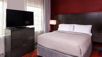 A hotel room with a large flat-screen TV on a dark wooden dresser, a bed with white linens, and a red accent wall.