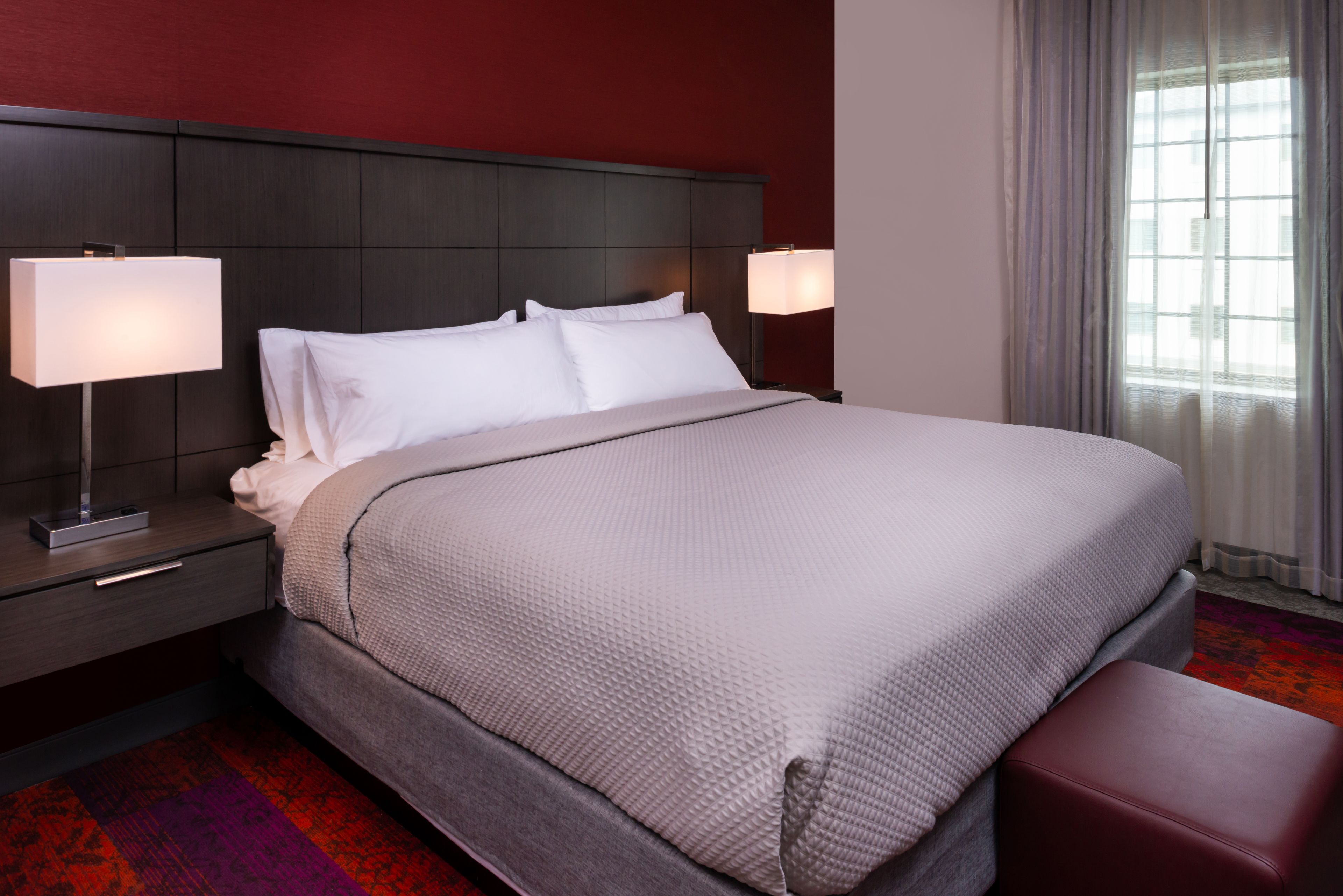 Una habitación de hotel con una cama grande, dos mesitas de noche y un ventanal con cortinas.