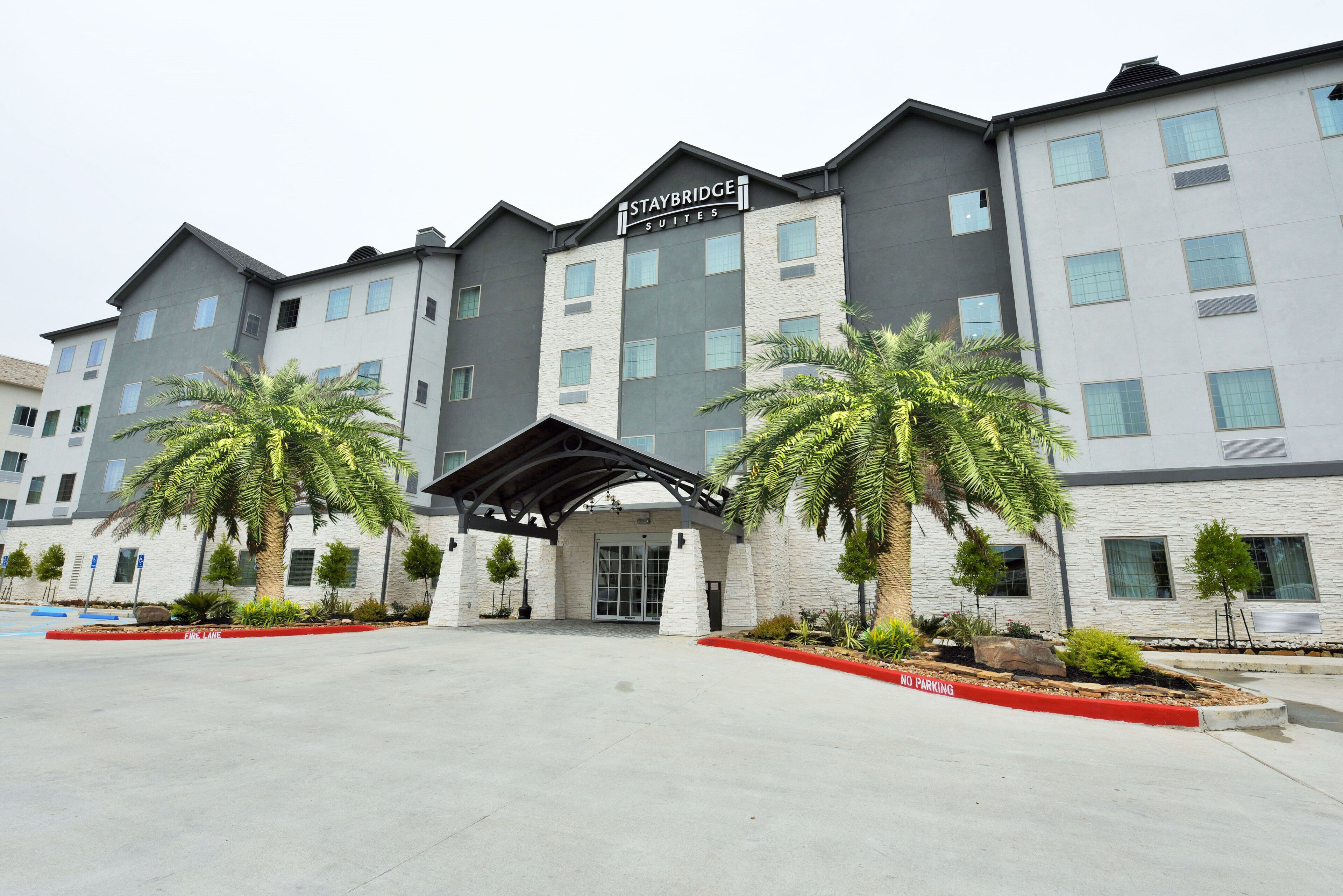 A Staybridge hotel with a modern facade, a covered entrance, and a landscaped entrance area with palm trees.