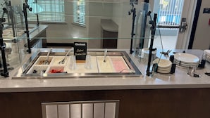 A buffet area with a sign reading "Chobani Custom Creation Bar," glass railings, and a view of the outside through the windows.