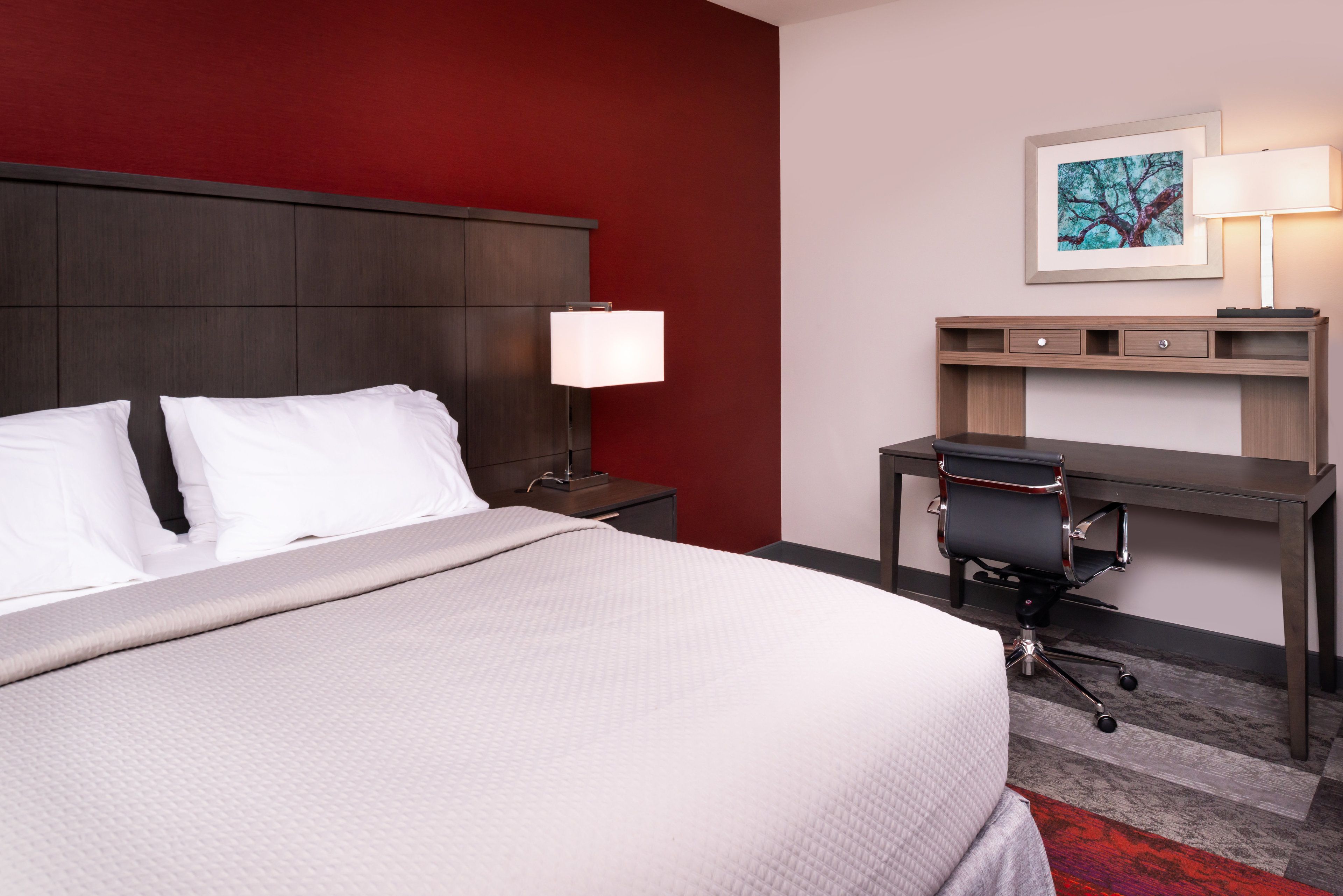 Une chambre d’hôtel avec un grand lit, un bureau avec une chaise, une table de chevet et une lampe.