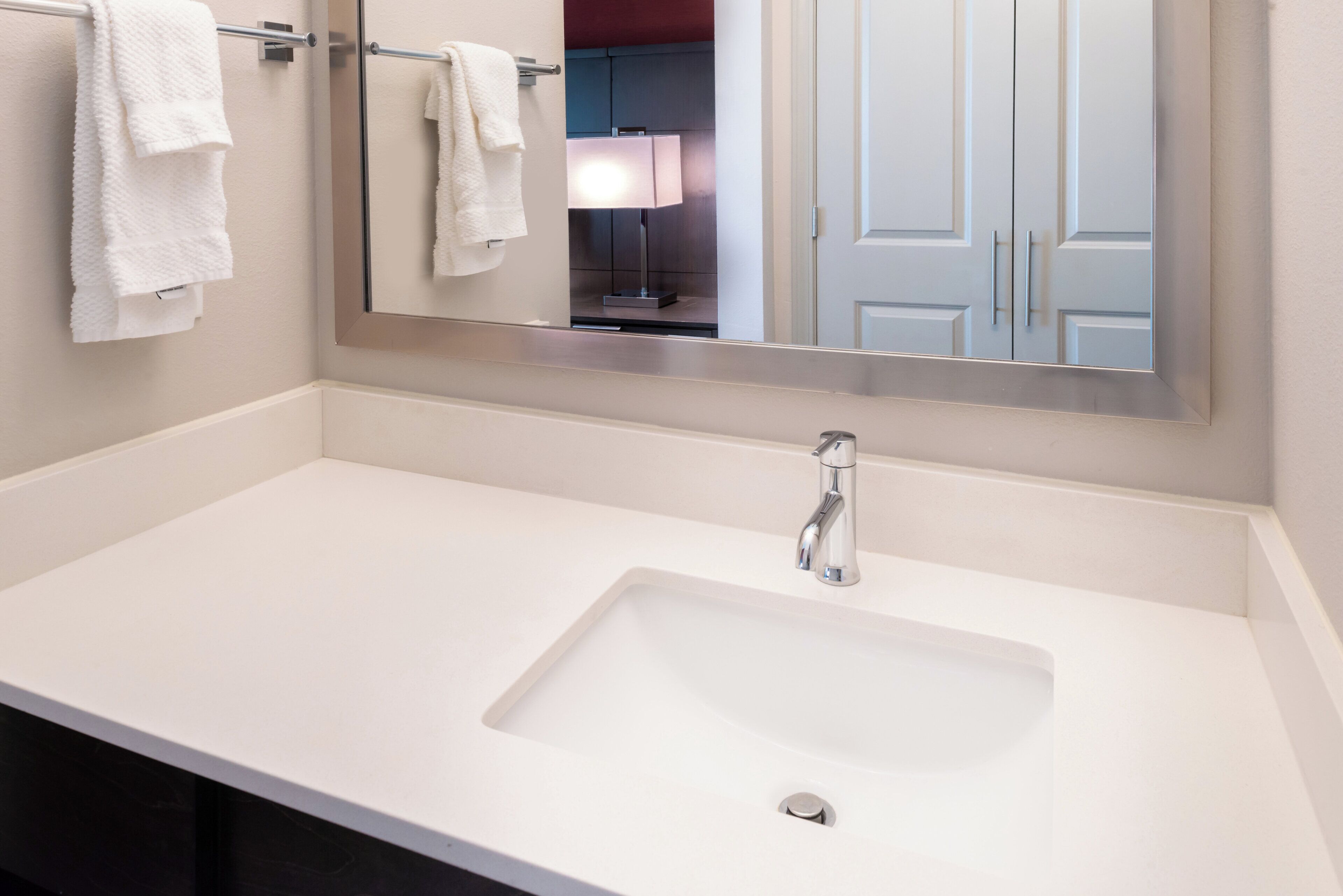 A bathroom with a white sink, a mirror, and two towels hanging on towel bars.