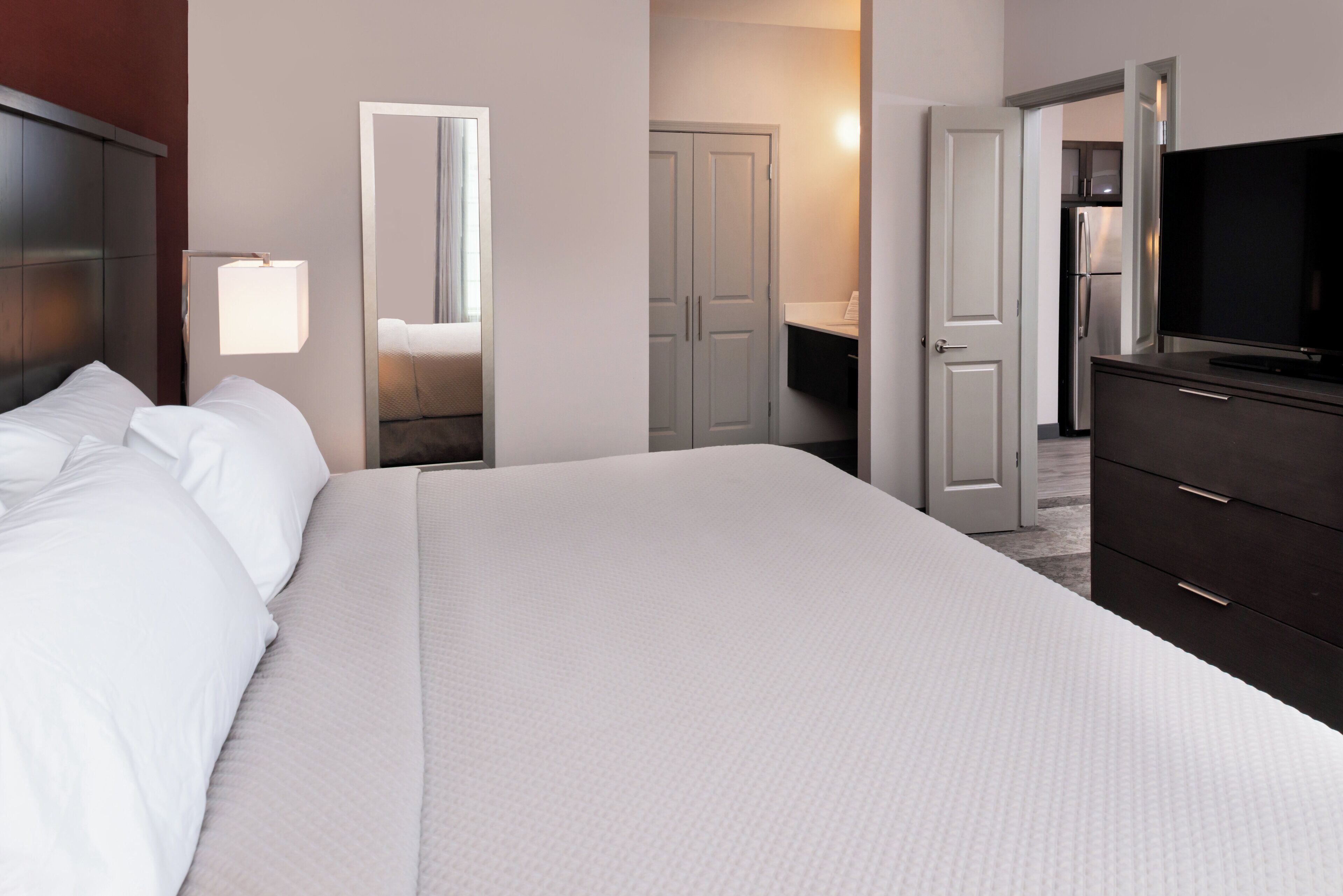A hotel room with a large bed, a dresser, a television, and a bathroom visible through an open door.