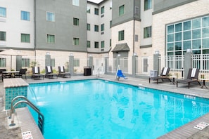 A swimming pool with lounge chairs and tables, surrounded by a building with multiple windows and a stone facade. - Staybridge Suites Lake Charles by IHG (Lake Charles)