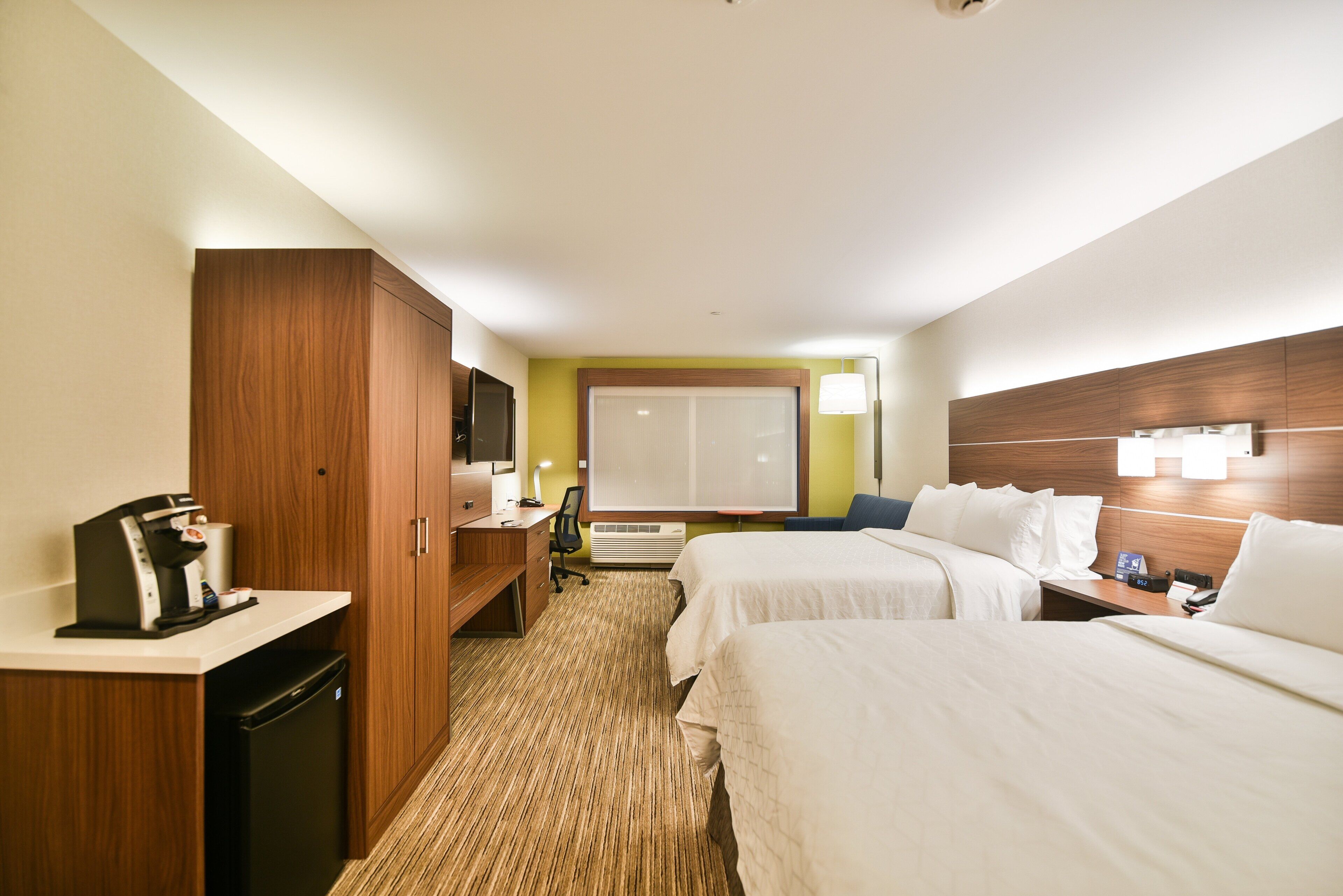 Una habitación de hotel con kitchenette, escritorio, dos camas y un amplio ventanal.