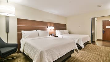 Habitación de hotel con dos camas, un escritorio, una silla y una lámpara.