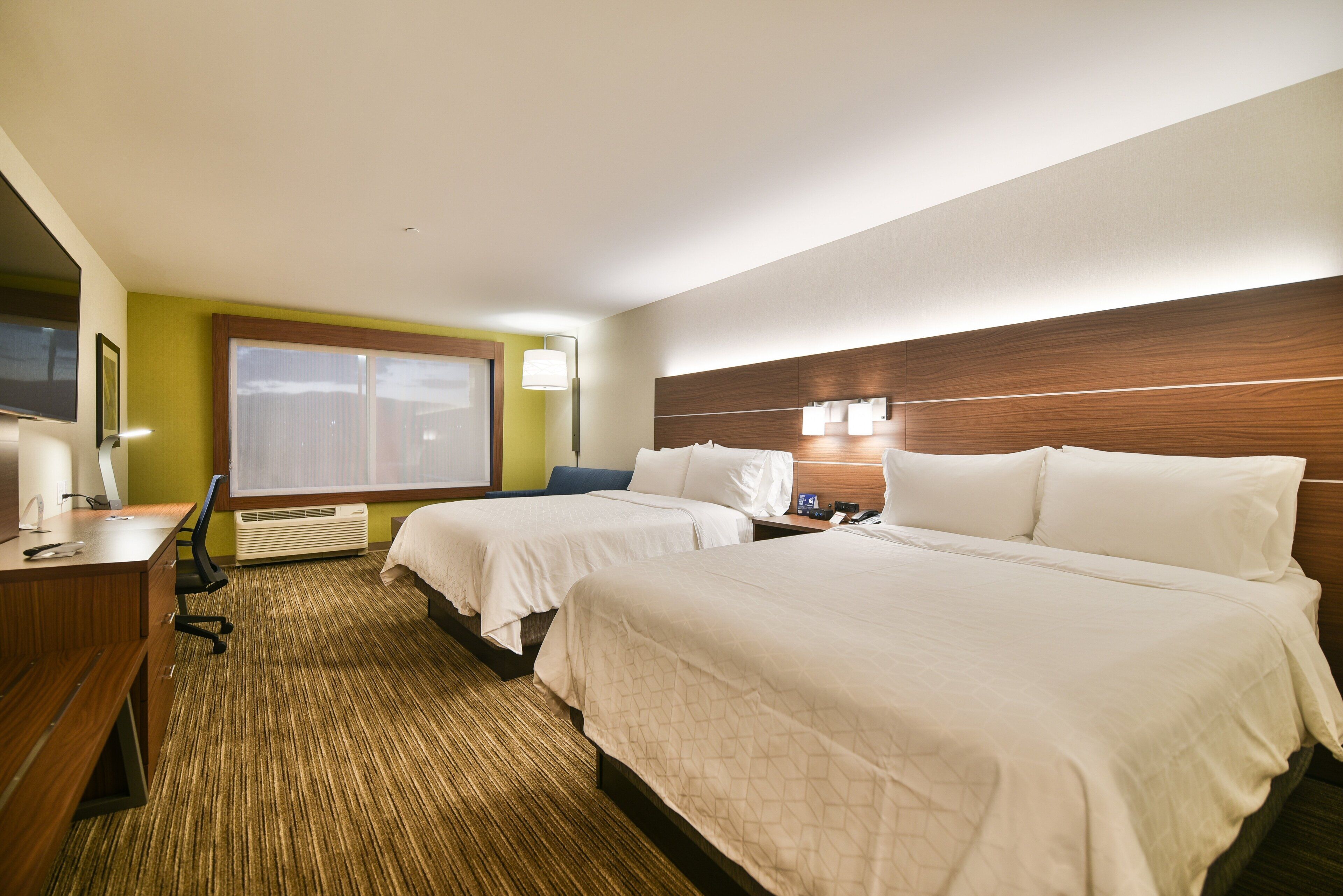 Une chambre d’hôtel avec deux lits, un bureau avec une chaise, une télévision et une fenêtre avec des stores.