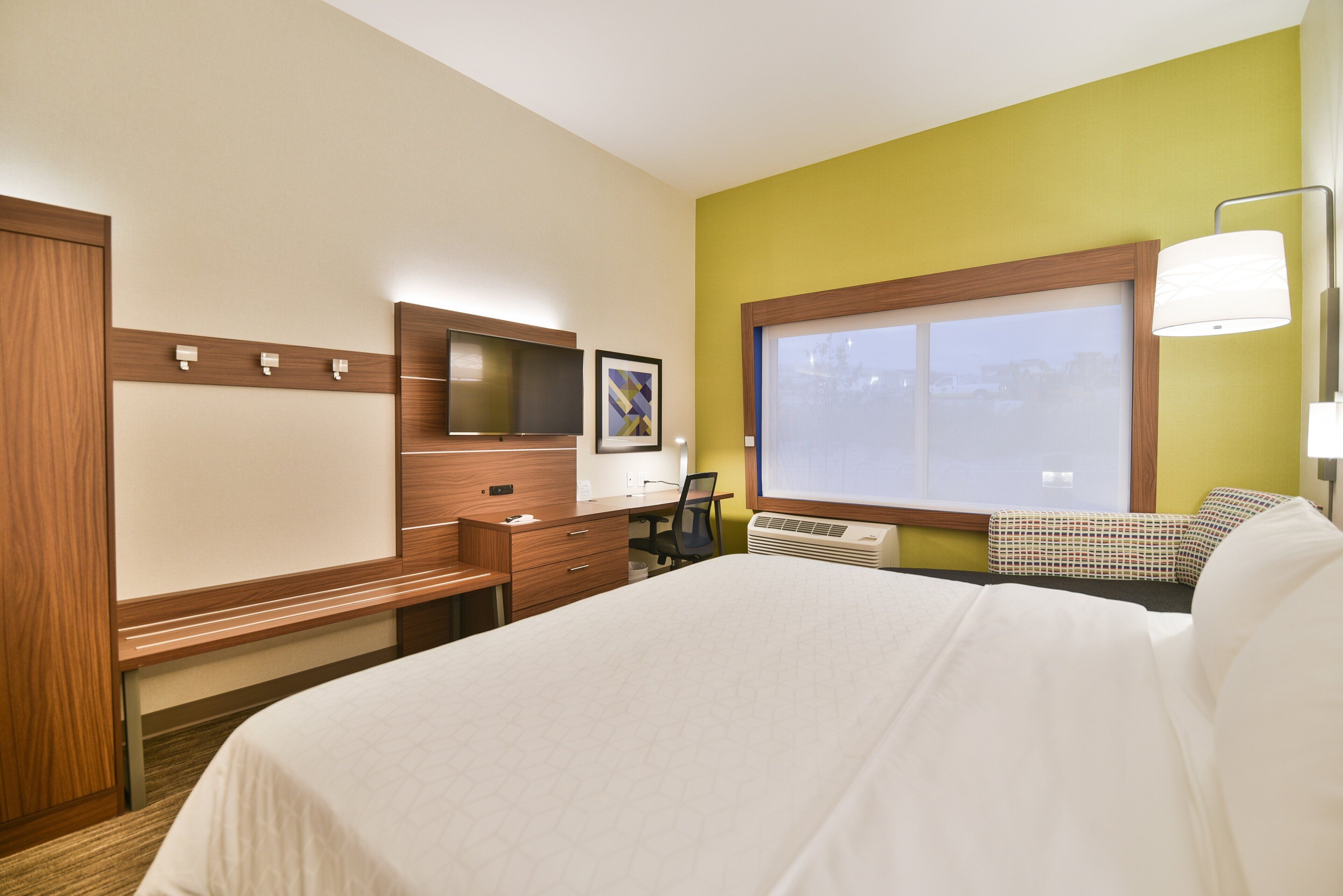 A hotel room with a bed, a desk, a chair, a TV, and a window.