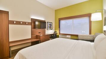 A hotel room with a bed, a desk, a chair, a TV, and a window.
