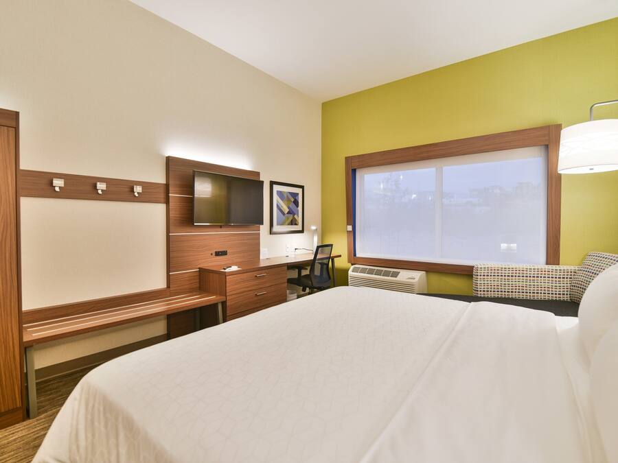 A hotel room with a bed, a desk, a chair, a TV, and a window.