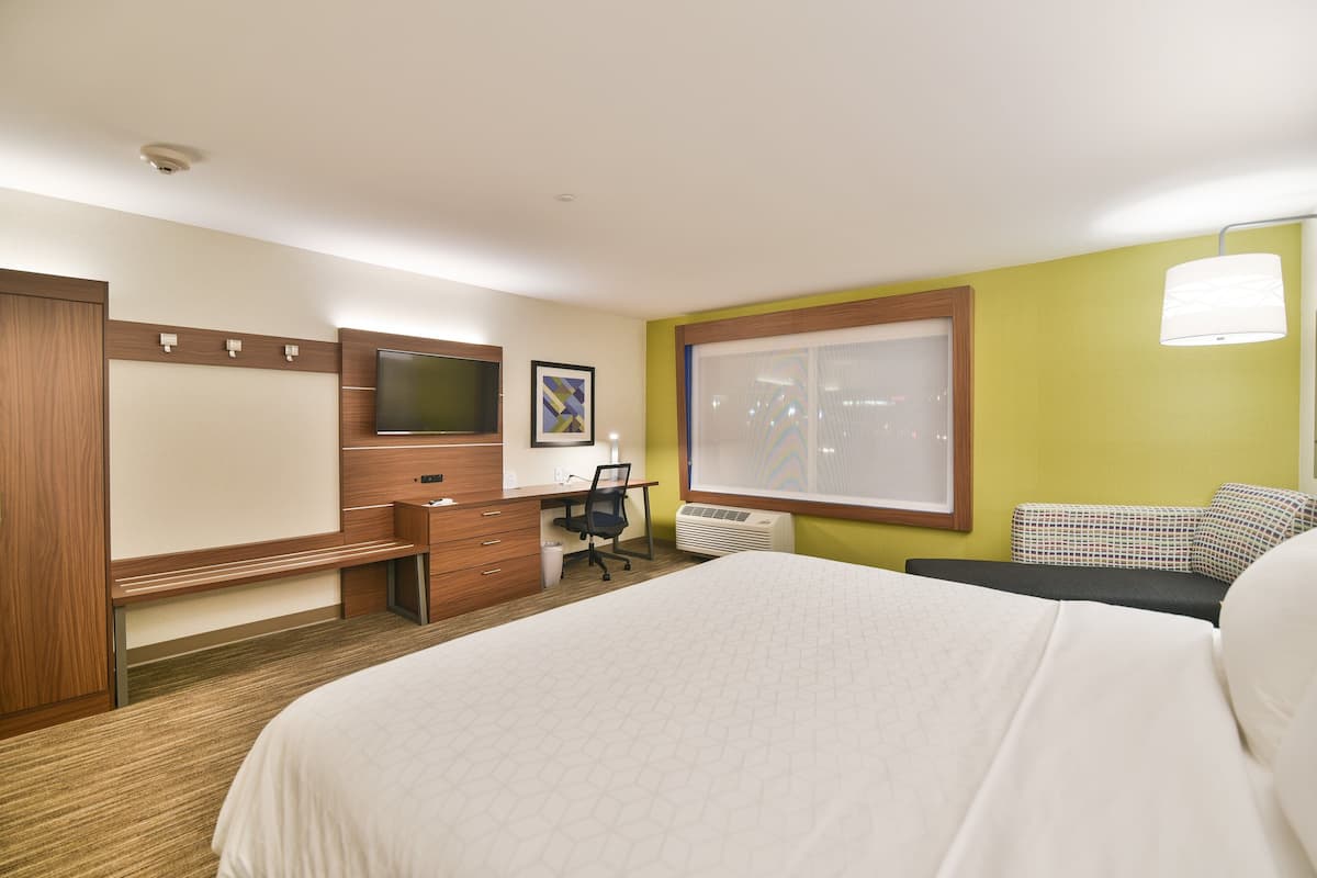 A hotel room with a large bed, a desk with a chair, a television, and a window with blinds.