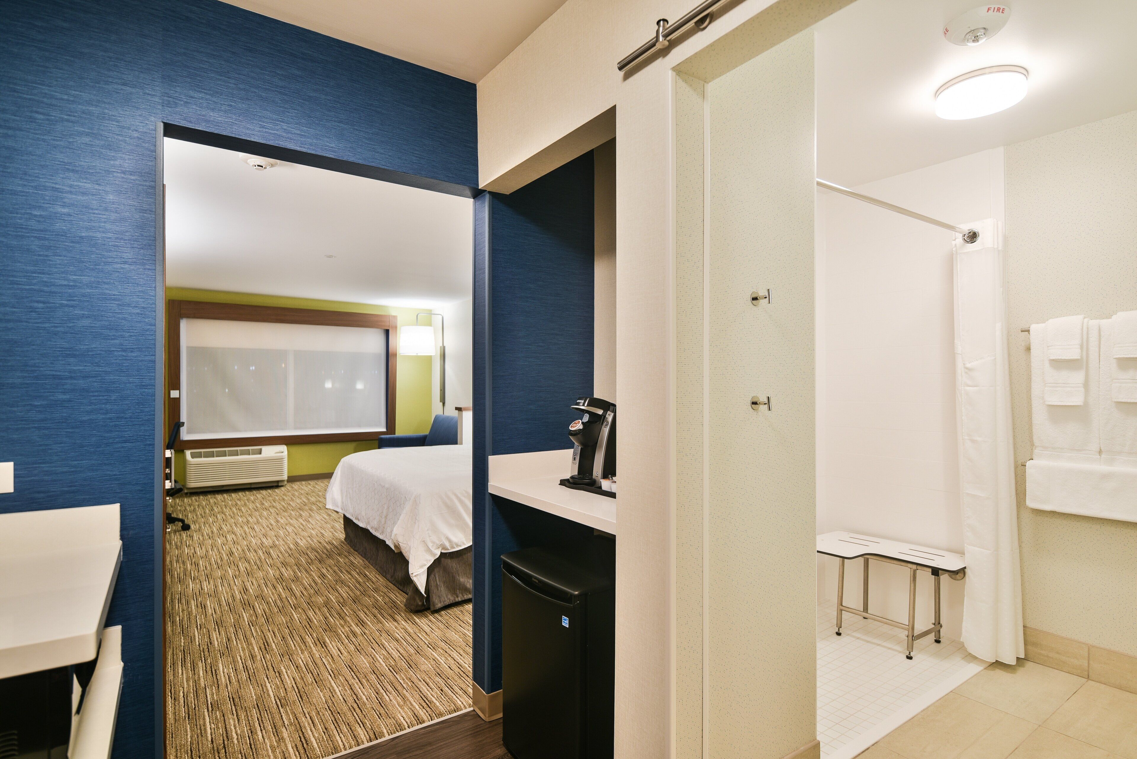 A hotel room with a bed, a desk, a coffee machine, and a shower area.