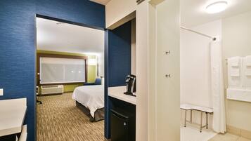 A hotel room with a bed, a desk, a coffee machine, and a shower area.