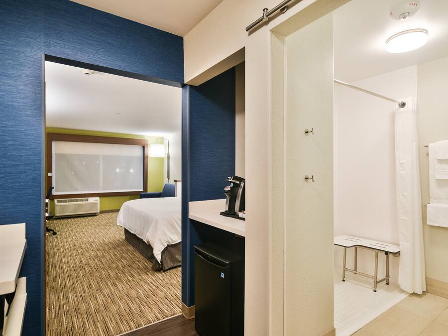 A hotel room with a bed, a desk, a coffee machine, and a shower area.