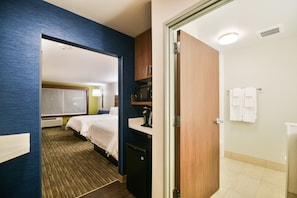 Quarto de hotel com cama, escrivaninha, micro-ondas e pequeno frigorífico.