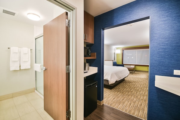 Quarto de hotel com chuveiro, cama, micro-ondas e pequena geladeira.