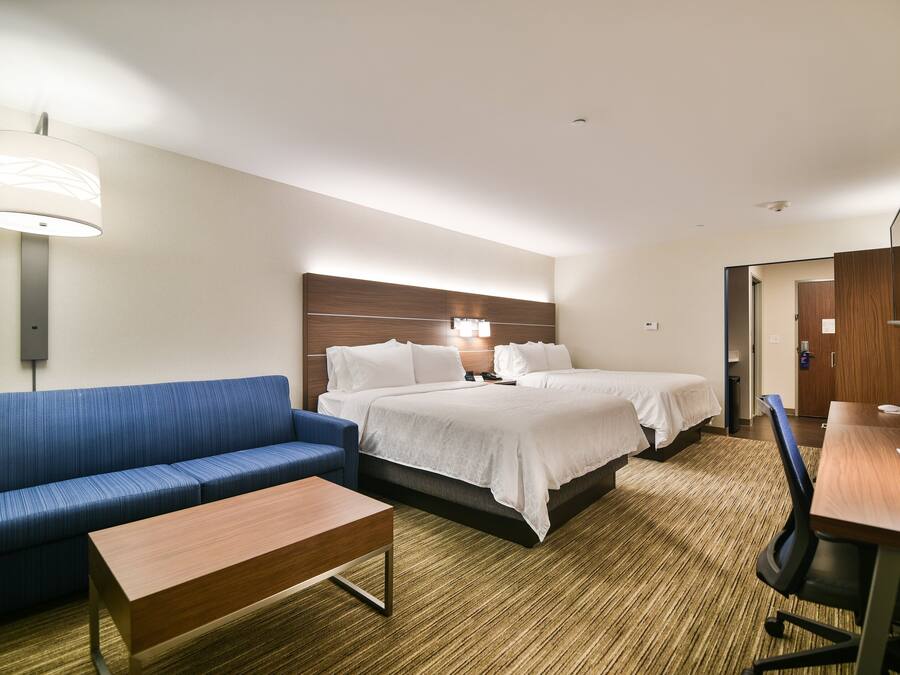Ein Hotelzimmer mit einem blauen Sofa, einem Holztisch, einem Doppelbett mit weißer Bettwäsche, einem Schreibtisch mit Stuhl und einer Wandlampe.