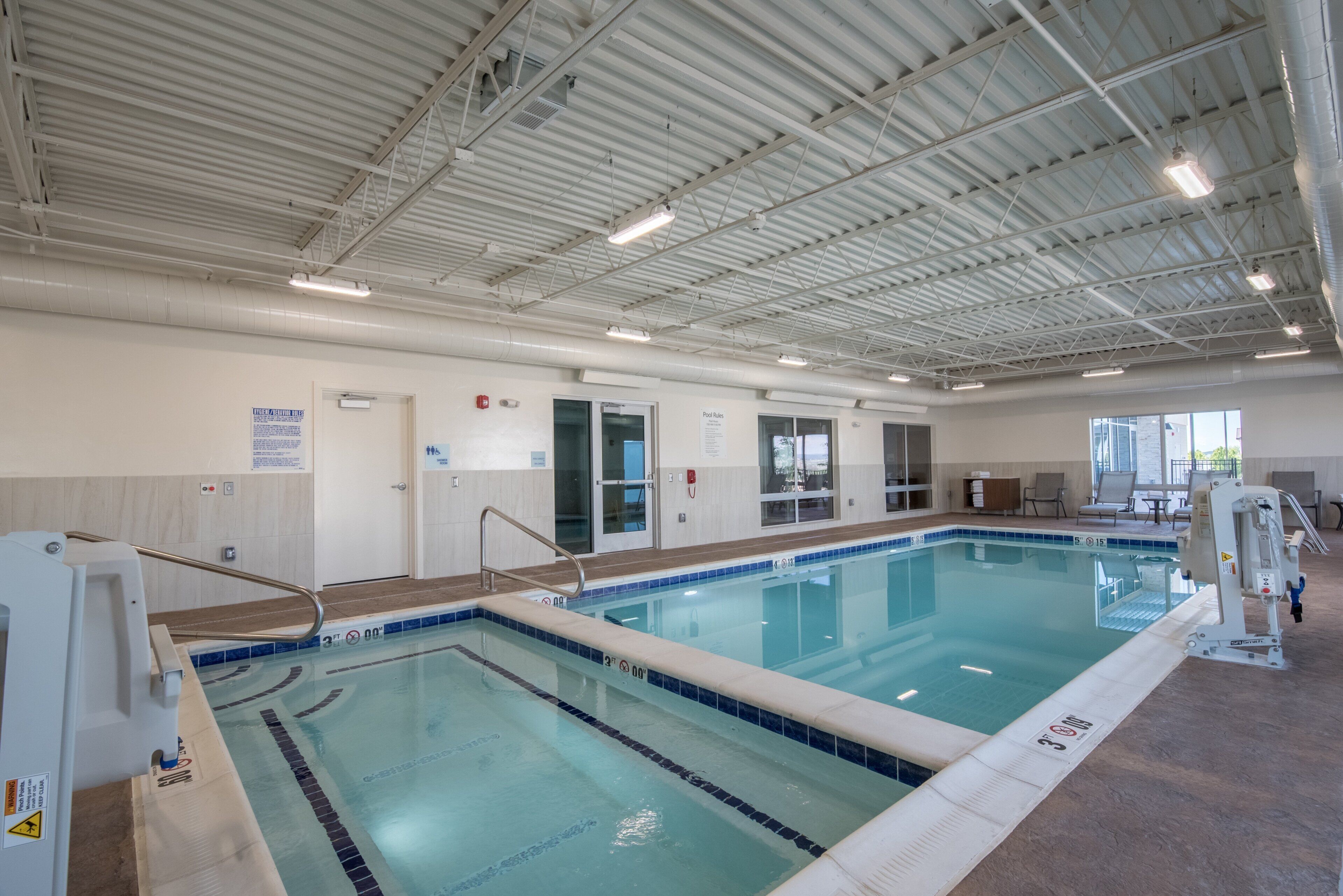 Una piscina techada con marcas de carril claras, una silla de salvavidas y un cartel con las normas de la piscina.