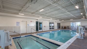 Ein Hallenbad mit deutlichen Bahnen, einem Rettungsschwimmerstuhl und einem Hinweisschild mit Poolregeln.