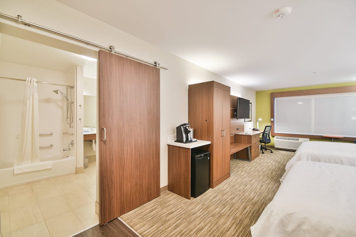 A hotel room with a shower, a desk, a bed, and a large window.
