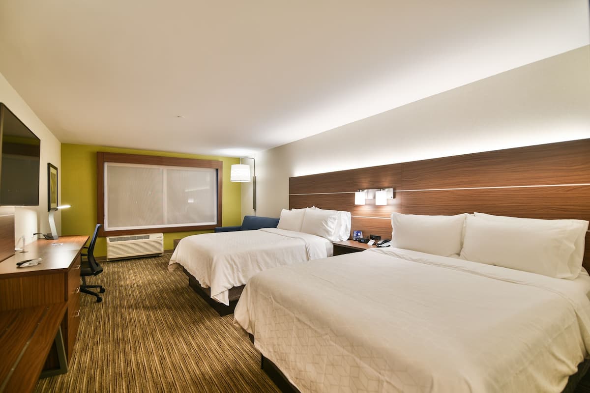 A hotel room with two beds, a desk, a chair, a large window, and a wall-mounted TV.