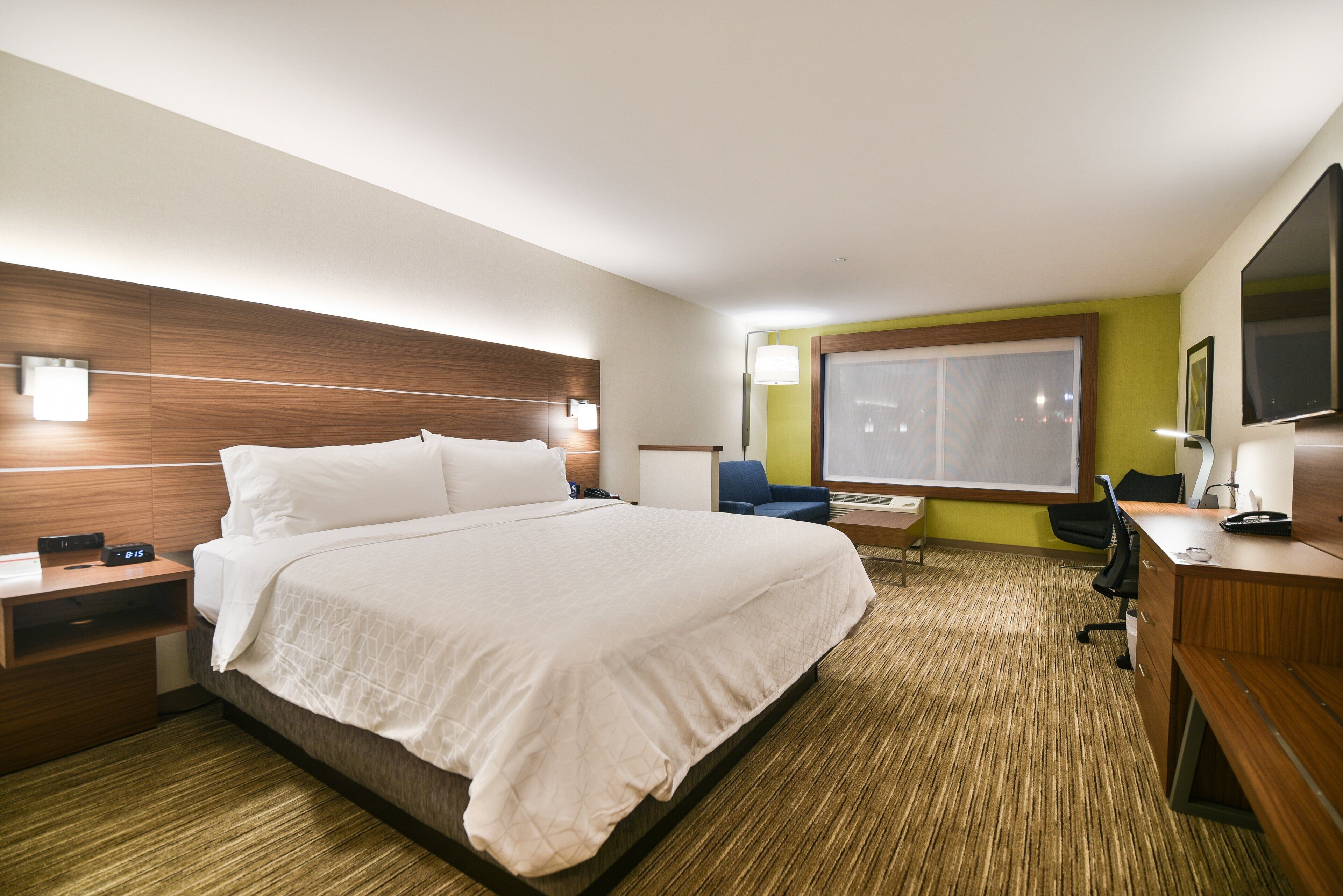 Habitación de hotel con una cama grande, mesitas de noche, un escritorio con silla, una ventana con persianas y un televisor de pantalla plana.