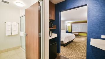 A hotel room with a bathroom, a bed, a desk, and a microwave.