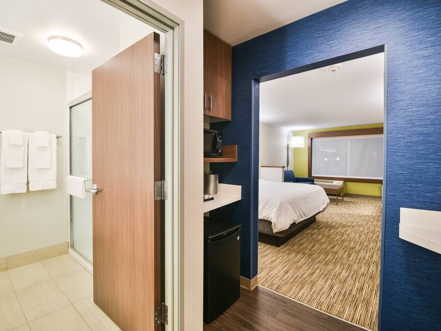 A hotel room with a bathroom, a bed, a desk, and a microwave.