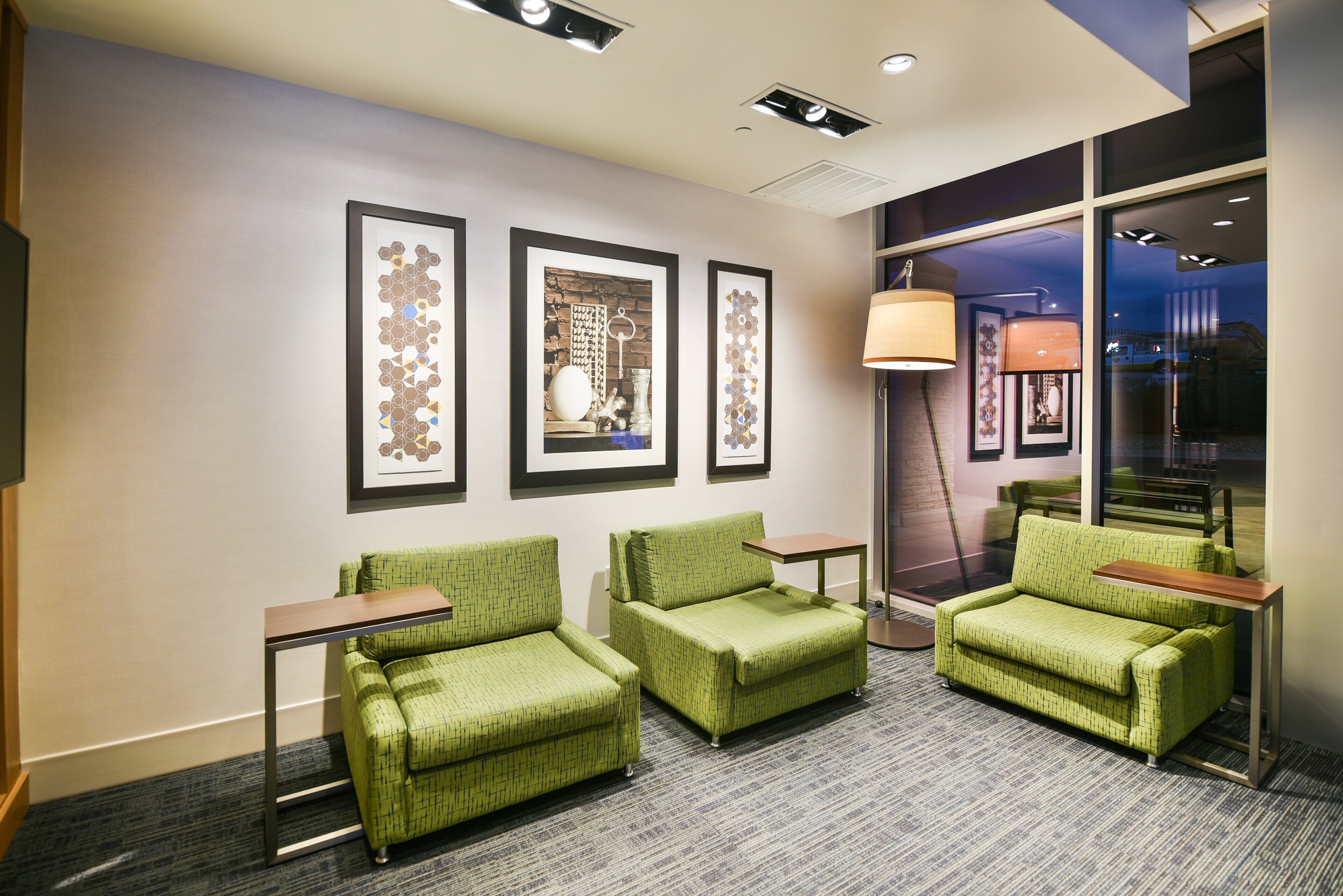 Un vestíbulo de hotel con tres sillones verdes, una mesita y obras de arte enmarcadas en la pared.