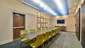 Uma sala de conferências com uma mesa comprida, cadeiras amarelas, uma televisão de tela plana e obras de arte emolduradas na parede.