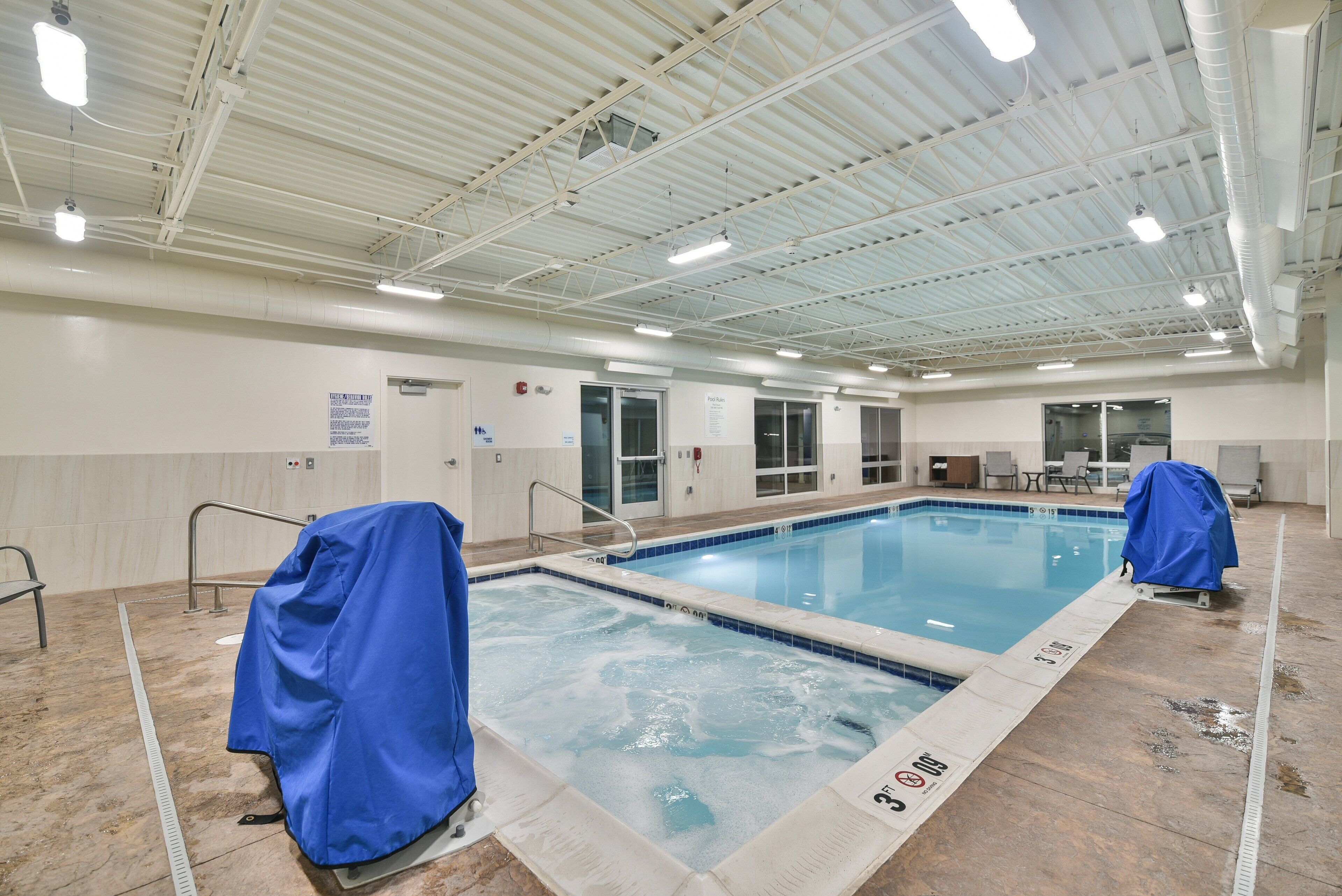 Una piscina interior con agua cristalina, paredes de azulejos y un techo alto con vigas estructurales visibles.