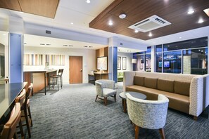 A modern hotel lobby with a reception desk, seating area, and a large window with a view.